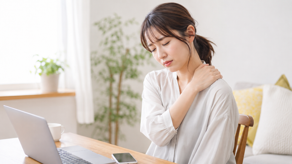 デスクでノートパソコンを前に肩に手を当てて痛みを訴える女性の写真